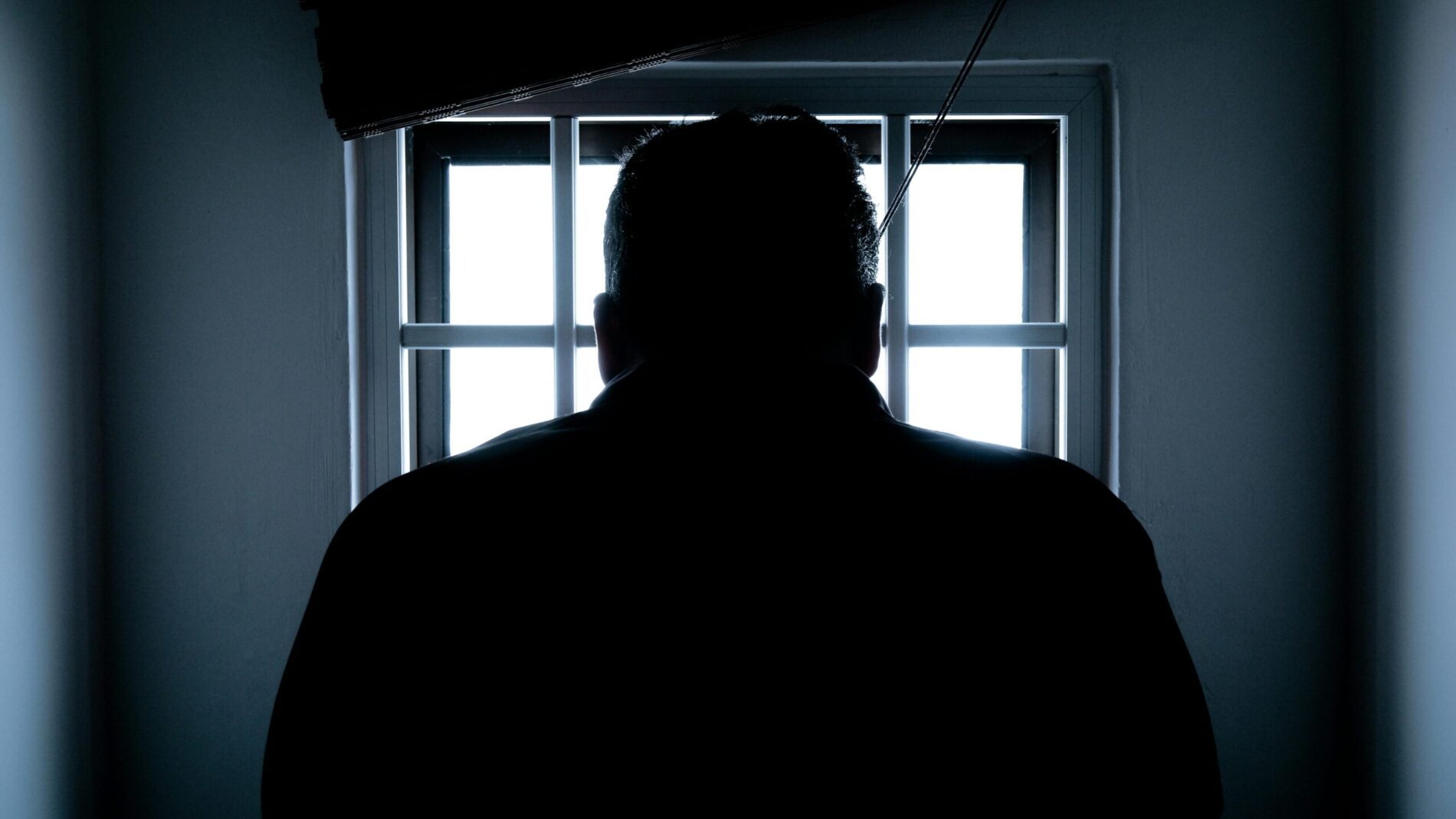 Mann steht vor einem vergitterten Fenster und blickt nach draußen