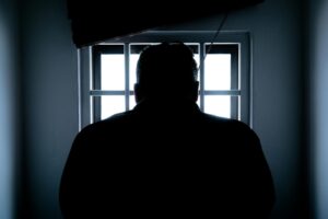 Mann steht vor einem vergitterten Fenster und blickt nach draußen